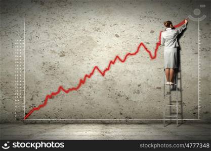 businesswoman drawing diagrams on wall. businesswoman standing on ladder drawing diagrams and graphs on wall