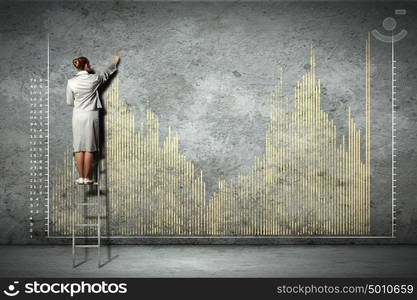 businesswoman drawing diagrams on wall. businesswoman standing on ladder drawing diagrams and graphs on wall