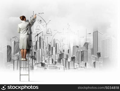 Businesswoman drawing on wall. Businesswoman standing on ladder and drawing sketch on wall