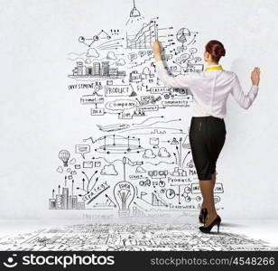 Businesswoman drawing on wall. Businesswoman standing with back drawing business ideas on wall