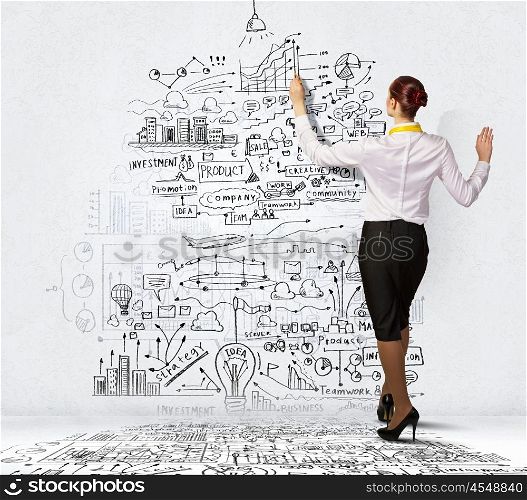 Businesswoman drawing on wall. Businesswoman standing with back drawing business ideas on wall