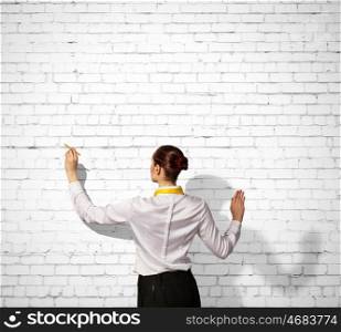 Businesswoman drawing on wall. Businesswoman standing with back drawing on blank wall