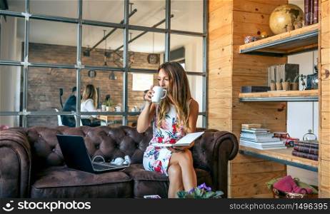 Businesswoman drinking coffee and working sitting on the sofa in a coworking office. Businesswoman drinking coffee and working in a coworking office