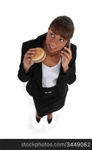 businesswoman eating a hamburger and talking on her cell