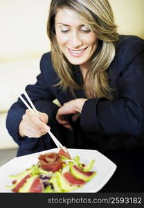 Businesswoman eating salad with chopsticks