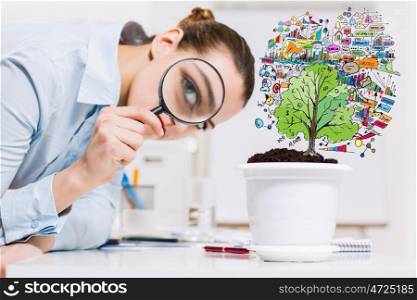 Businesswoman examining sprout. Young businesswoman looking at drawn image of sprout through magnifier
