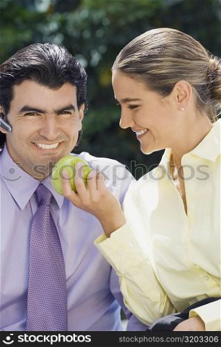 Businesswoman feeding a green apple to a businessman and smiling