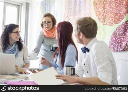 Businesswoman giving coffee to colleagues in creative office