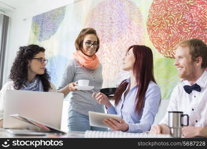 Businesswoman giving coffee to female colleague in creative office