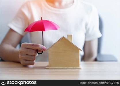 Businesswoman hand holding red Umbrella cover wooden Home model. real estate, insurance and property concepts