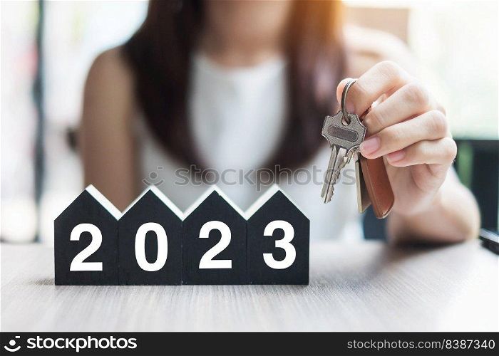 Businesswoman hands holding key and 2023 Happy New Year with house model on table office. New House, Financial, Property insurance, real estate, savings and New Year Resolution concepts