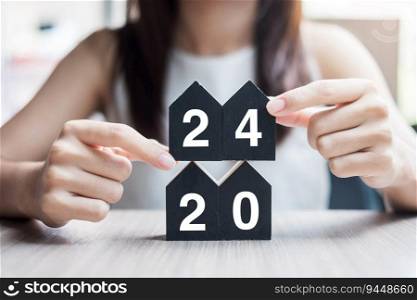 Businesswoman hands holding key and 2024 Happy New Year with house model on table office. New House, Financial, Property insurance, real estate, savings and New Year Resolution concepts