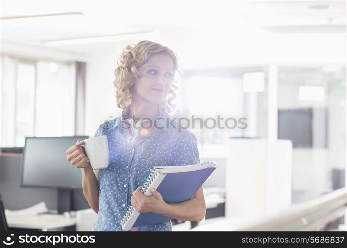 Businesswoman having coffee while holding files in creative office