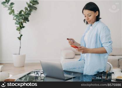 Businesswoman holding bank credit card and smartphone, using online banking services, e-bank apps, making secure payment on payday at workplace, sitting on office desk. Ebusiness, e commerce concept.. Female holds bank credit card, phone uses online banking service at workplace. E-business, ecommerce