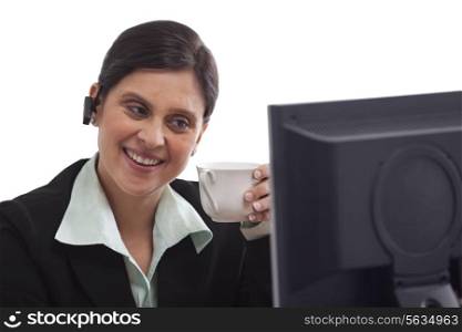 Businesswoman holding coffee cup while looking at computer
