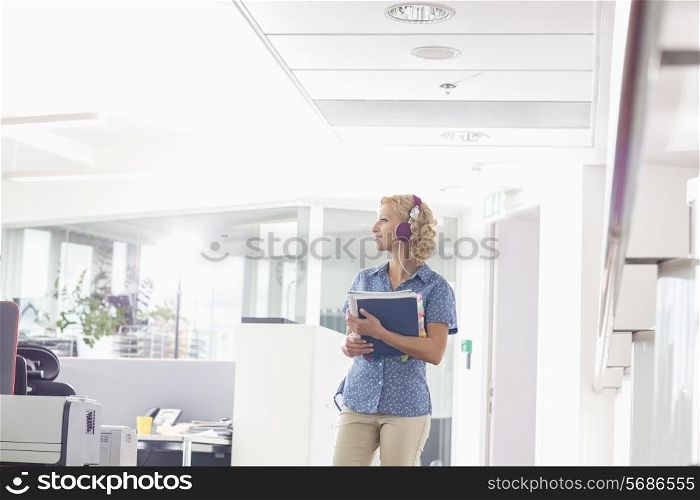 Businesswoman holding files while listening music in creative office