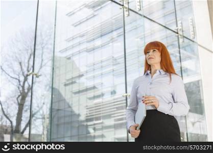 Businesswoman holding laptop by glass wall in office
