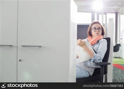 Businesswoman holding notepad while sitting on chair at creative office