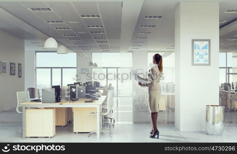 Businesswoman holding paper sheets mixed media. Young elegant businesswoman in office interior with documents in hands