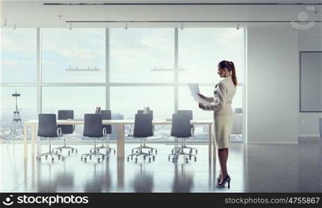 Businesswoman holding paper sheets mixed media. Young elegant businesswoman in office interior with documents in hands
