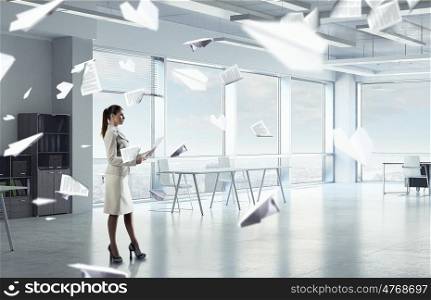Businesswoman holding paper sheets mixed media. Young elegant businesswoman in office interior with documents in hands