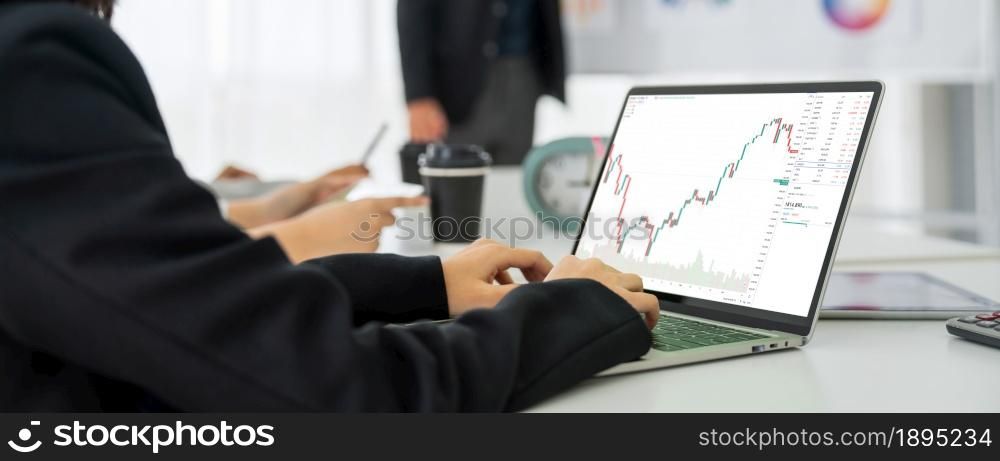 Businesswoman in analyze stock market data using laptop computer proficiently at the office while attending a group meeting with business team .. Businesswoman in analyze stock market data using laptop computer proficiently