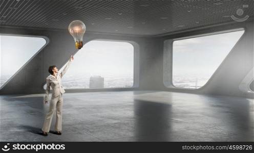 Businesswoman in building interior. Businesswoman in modern interior reaching hand to touch light bulb