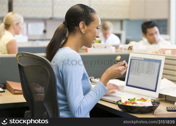 Businesswoman in cubicle eating sushi smiling