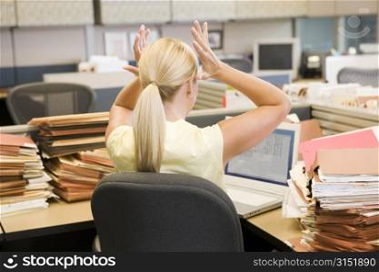 Businesswoman in cubicle with laptop and stacks of files