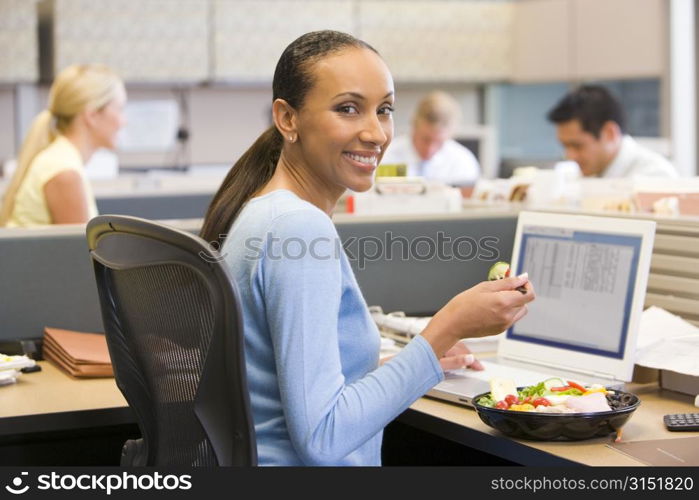 Businesswoman in cubicle with laptop eating salad