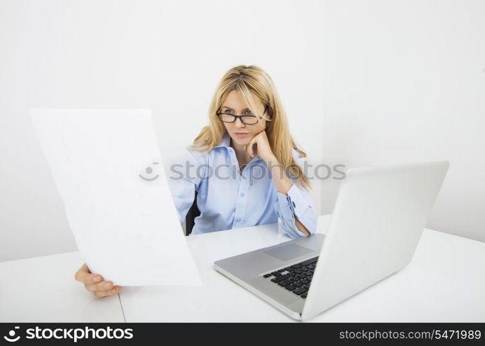 Businesswoman in eyeglasses reading document at office desk