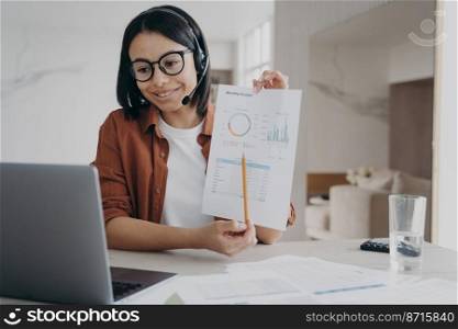 Businesswoman in headset showing chart, discussing business project while online video conference at laptop. Female manager makes presentation of financial report, working remotely. Remote job concept. Businesswoman in headset showing chart, discussing business project while video conference at laptop
