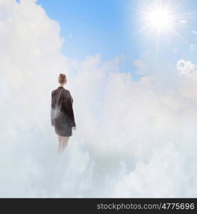 Businesswoman in heaven. Rear view of businesswoman standing on cloud high in sky