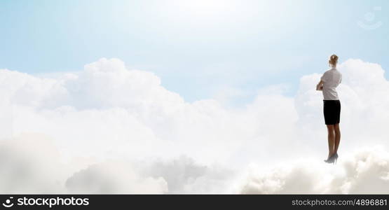 Businesswoman in heaven. Rear view of businesswoman standing on cloud high in sky