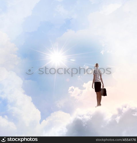 Businesswoman in heaven. Rear view of businesswoman with suitcase standing on cloud