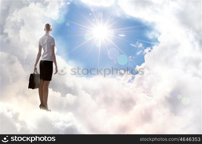 Businesswoman in heaven. Rear view of businesswoman with suitcase standing on cloud