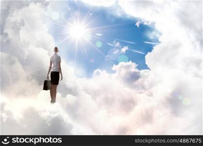 Businesswoman in heaven. Rear view of businesswoman with suitcase standing on cloud