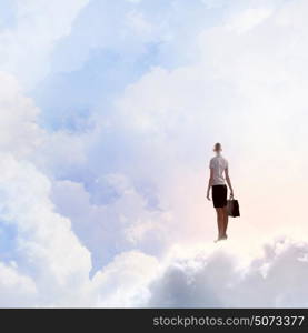 Businesswoman in heaven. Rear view of businesswoman with suitcase standing on cloud