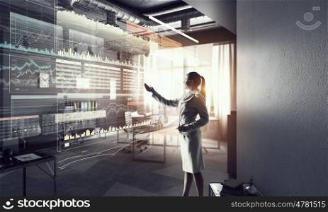 Businesswoman in modern office mixed media. Young elegant businesswoman in office working with virtual panel