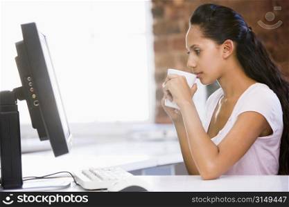 Businesswoman in office drinking coffee and looking at computer