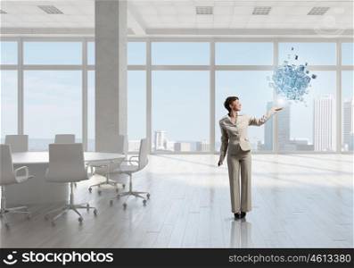 Businesswoman in office mixed media. Young successful businesswoman in white office interior and 3d cube figure in hand