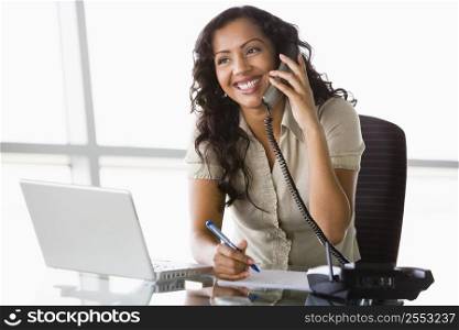Businesswoman in office on telephone by laptop smiling (high key/selective focus)