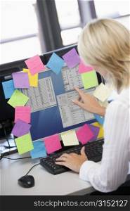 Businesswoman in office pointing at monitor with notes on it
