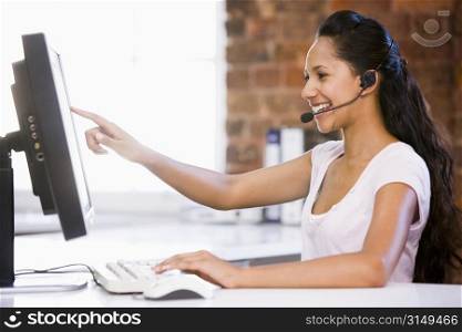 Businesswoman in office wearing headset and pointing at computer monitor