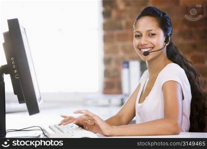 Businesswoman in office wearing headset and typing on computer smiling
