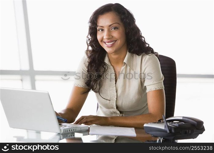 Businesswoman in office with laptop smiling (high key/selective focus)
