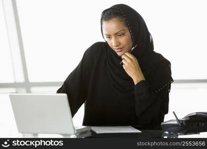 Businesswoman in office with laptop thinking (high key/selective focus)