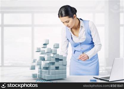 Businesswoman in process of work. Young attractive businesswoman working at her desk with laptop and 3D cube illustration