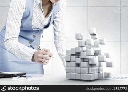 Businesswoman in process of work. Young attractive businesswoman working at her desk with laptop and 3D cube illustration
