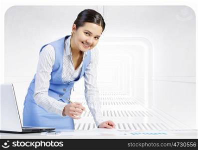 Businesswoman in process of work. Young attractive businesswoman working at her desk with laptop and papers